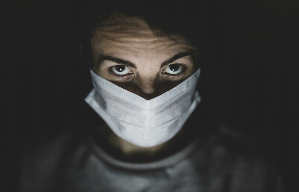 Man in the dark with a white medical mask on.